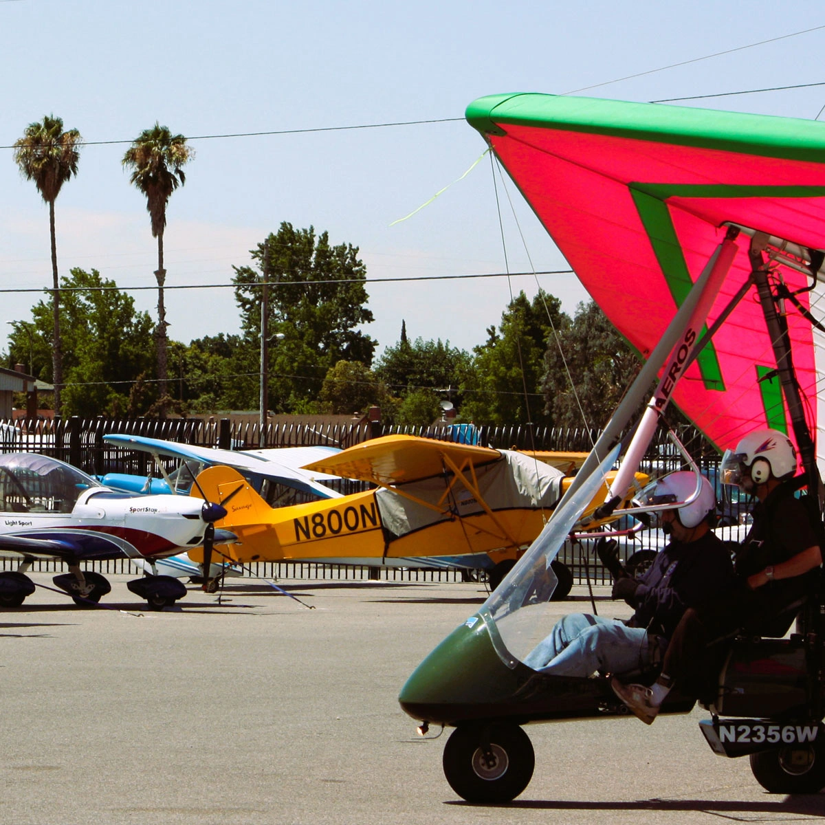 Several light sport aircraft and an ultralight trike parked at an airfield, showcasing their diverse designs and colors