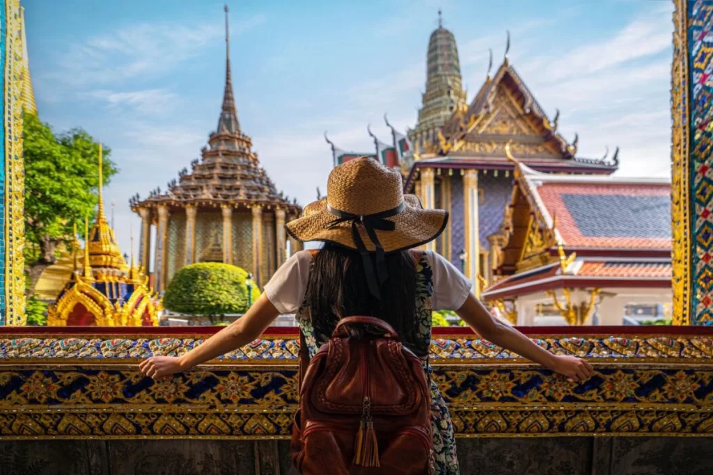 An American tourist exploring the intricate carvings and golden decorations of a temple inside the Grand Palace in Bangkok, Thailand