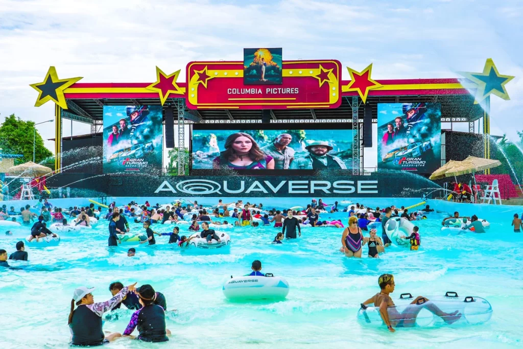 Visitors enjoying the wave pool at Columbia Pictures Aquaverse with large movie screens in the background showing scenes from popular Columbia Pictures films