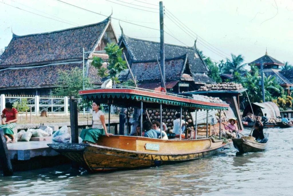 A colorful boat at Damnoen Saduak Floating Market, filled with fresh fruits, vegetables, and traditional Thai snacks, surrounded by other bustling boats on the canal