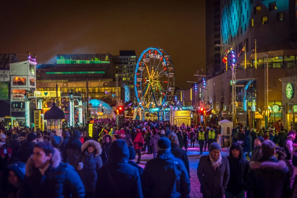 Crowds enjoying the Montreal en Lumière festival with colorful lights, a Ferris wheel, and illuminated installations, creating a vibrant winter night atmosphere