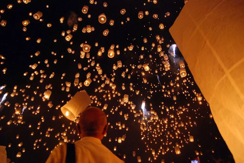 A crowd releasing glowing lanterns into the starry sky during the Yi Peng Lantern Festival in Chiang Mai, Thailand