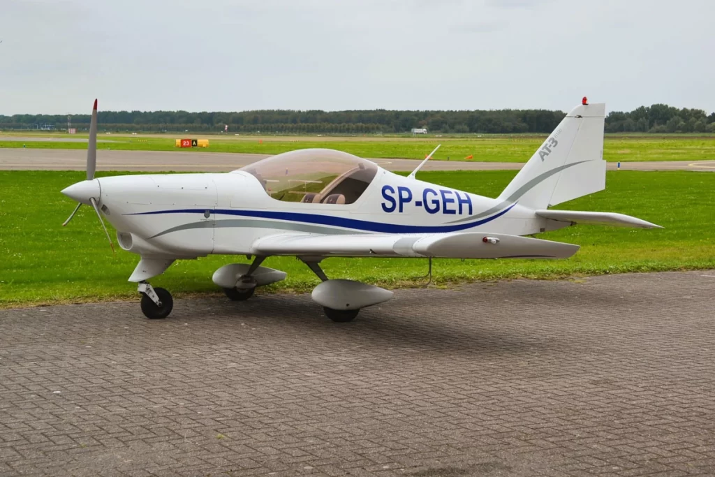 Aero AT-3 R100 parked on a tarmac near a grassy airfield, showcasing its aerodynamic and compact design