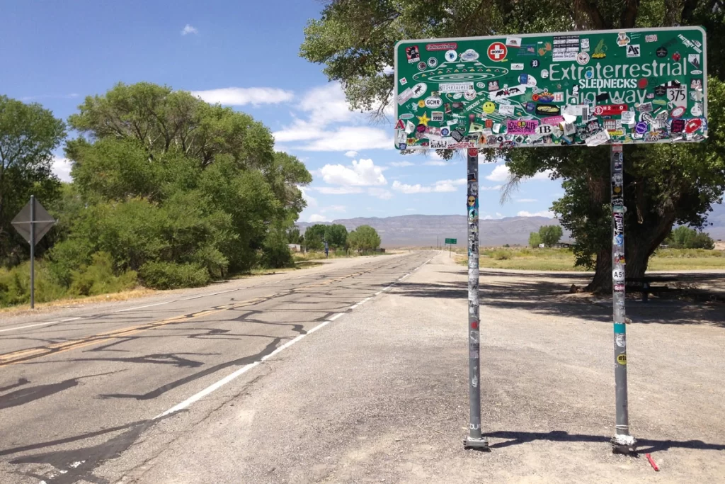 A scenic view of the Extraterrestrial Highway in Nevada with alien-themed road signs and a vast desert landscape under a clear blue sky.