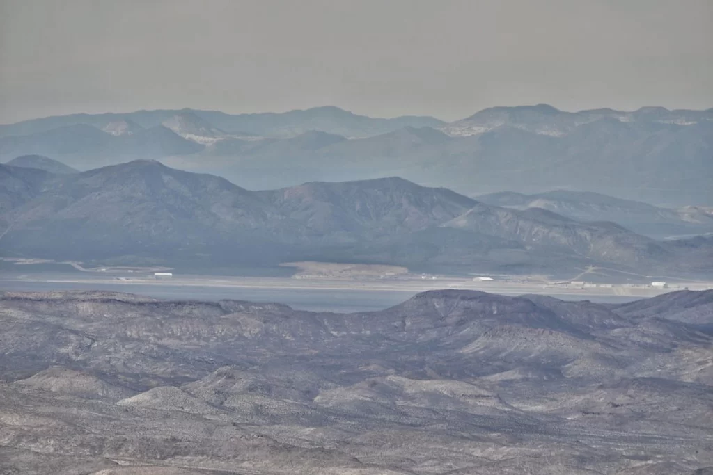 A panoramic view from Tikaboo Peak in Nevada, showcasing the vast desert and the distant Area 51 facility under a clear sky.