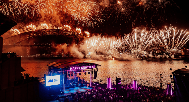 A dazzling fireworks display over Sydney Harbour with the iconic Opera House and Harbour Bridge in view, accompanied by live music performances.