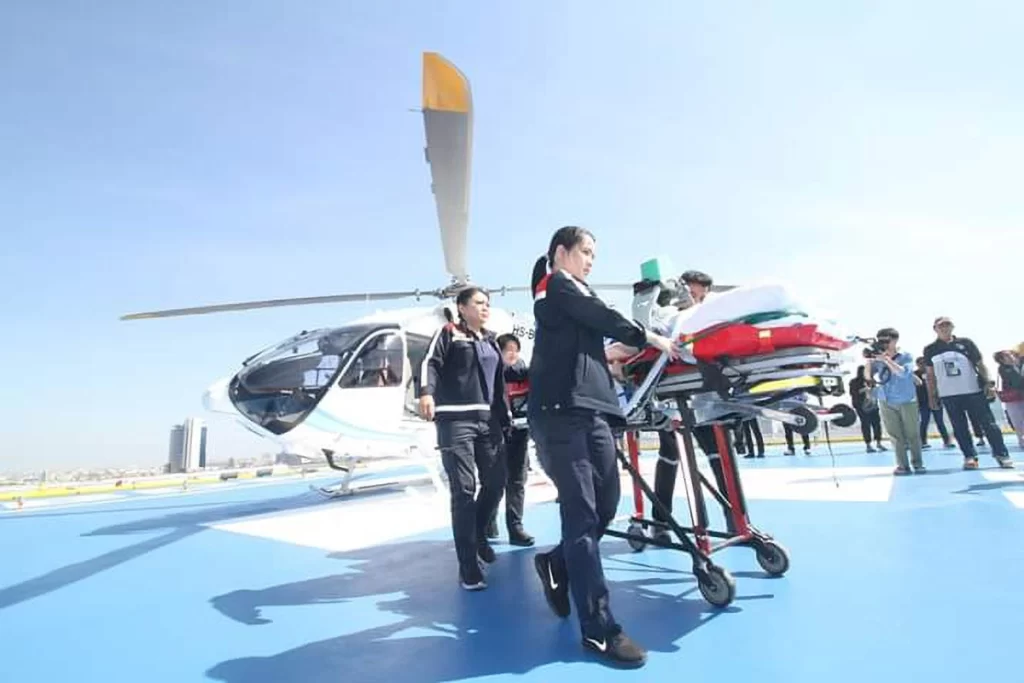 Emergency medical team transferring a patient via air ambulance helicopter at a hospital helipad in Thailand