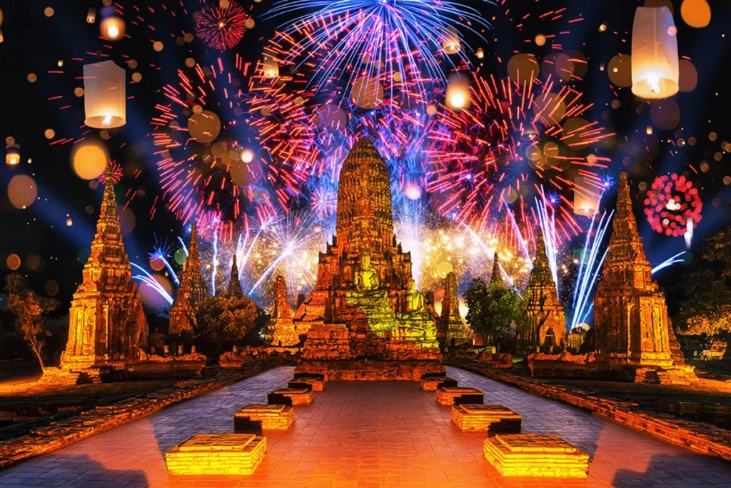 A vibrant nighttime scene at Ayutthaya Historical Park featuring illuminated ancient temple ruins, colorful fireworks lighting up the sky, and floating lanterns adding a magical ambiance.