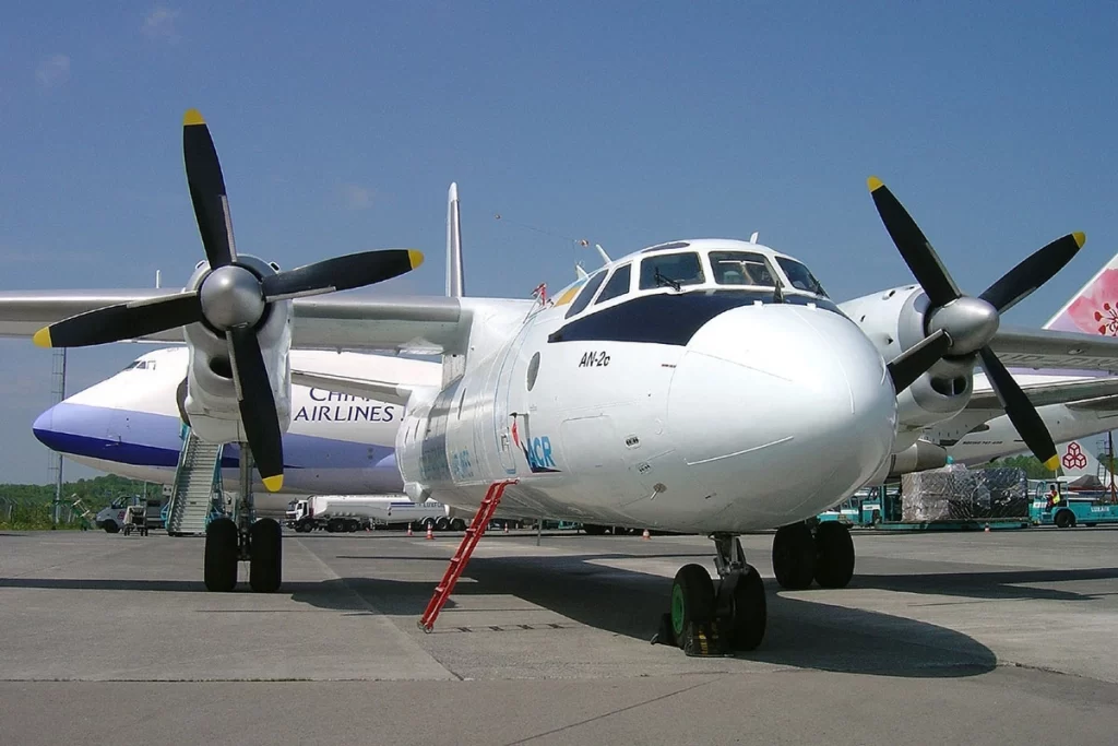 A close-up view of a white twin-engine turboprop aircraft parked on the runway, featuring large propellers