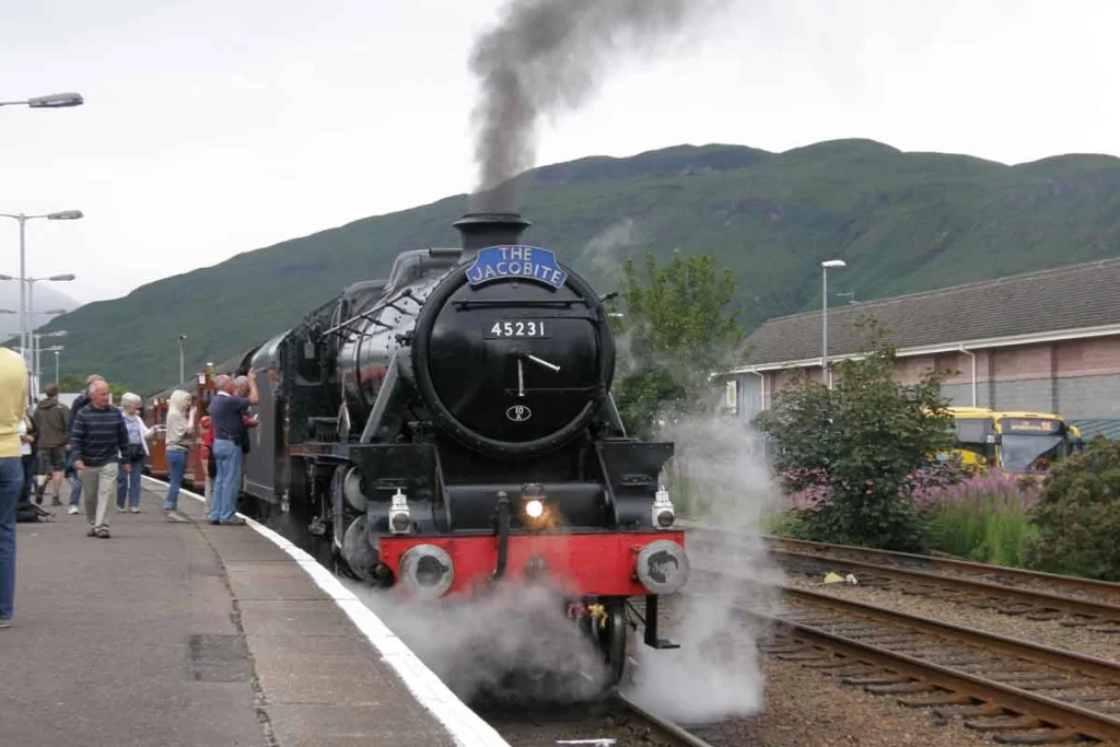 A vintage steam train crossing the Glenfinnan Viaduct in the Scottish Highlands, often recognized as the Hogwarts Express from the Harry Potter films.