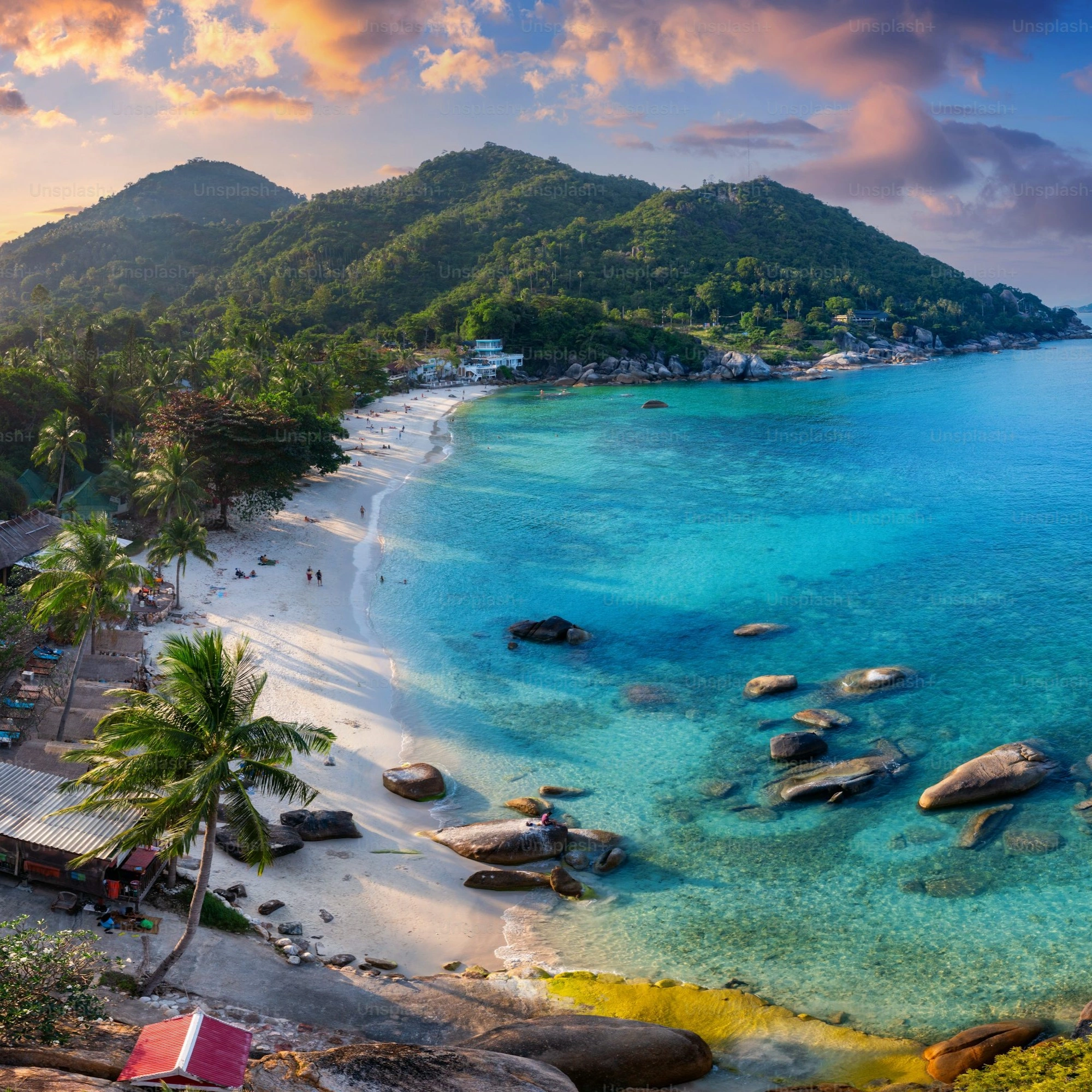 Scenic aerial view of a tropical beach with turquoise waters, white sand, palm trees, and lush green mountains in Phuket, Thailand