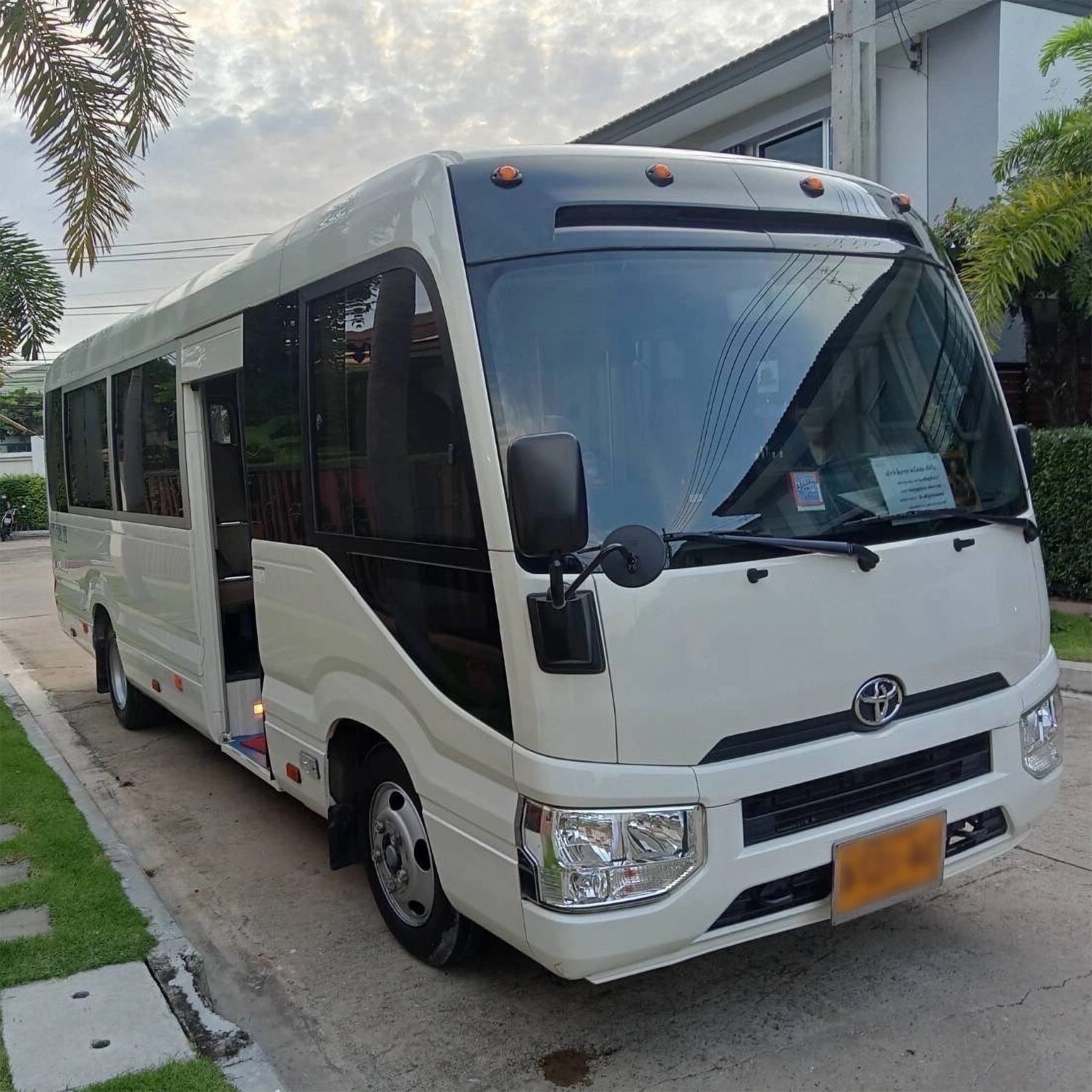 A white Toyota Coaster minibus parked on the roadside, ready for rental and group travel.