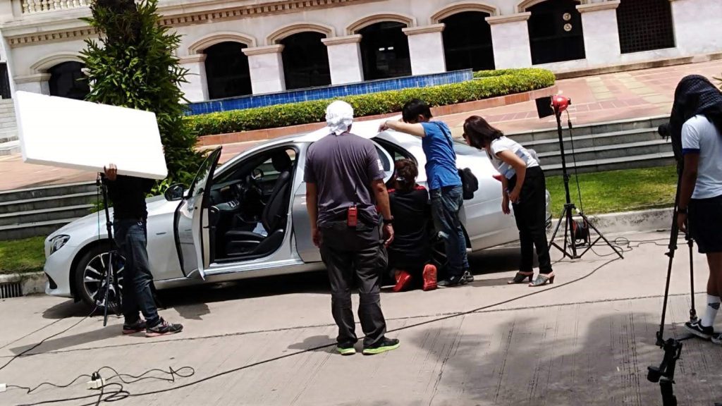 Film production crew preparing a luxury car for a scene, using THAITAXISERVICES™ vehicle rental