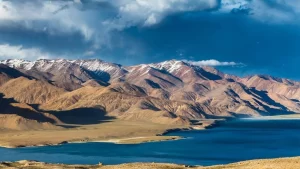 A scenic view of the Pamir Mountains and a deep blue lake under a cloudy sky at Irkeshtam Pass, an ancient route to Central Asia