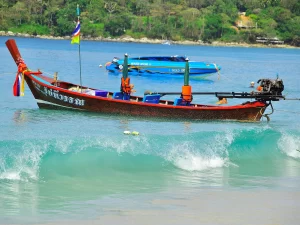 A traditional Thai longtail boat floating near the shore with crystal-clear waves in Phuket