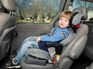 A young boy sitting in a high-back booster seat inside a car, securely fastened with a seat belt