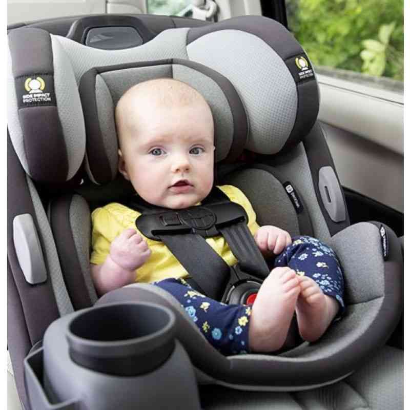 A baby sitting securely in a rear-facing infant car seat with a five-point harness inside a vehicle.